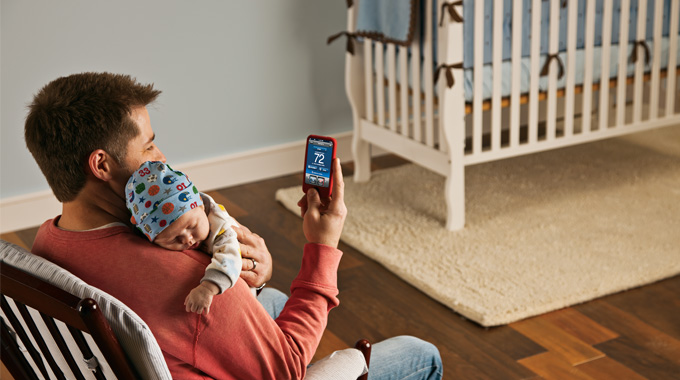 Father holding a baby while adjusting the temperature with his phone